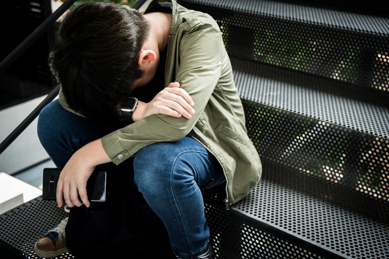 Adolescente asiatico seduto sulle scale a faccia in giù con lo smartphone in mano
