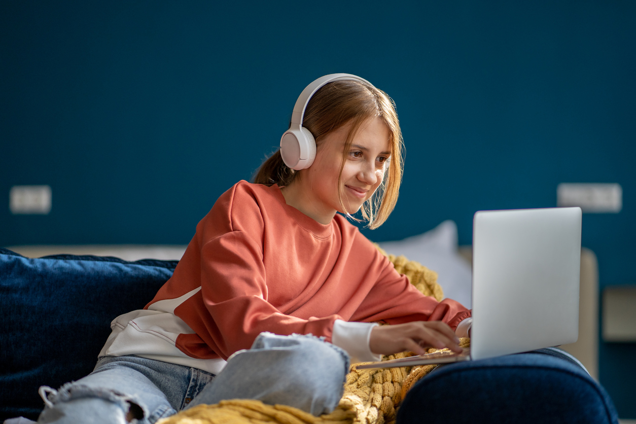 Adolescente sorridente scrive al computer mentre ascolta musica in cuffia