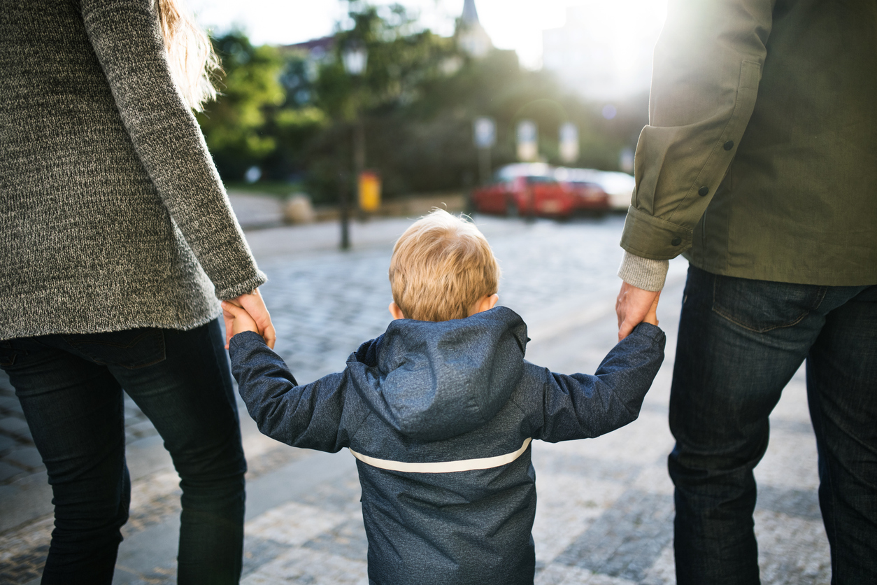 Un bambino cammina tenendo per mano i suoi genitori