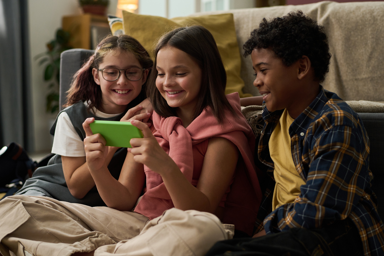 Due bambine e un bambino guardano insieme un cellulare sorridenti