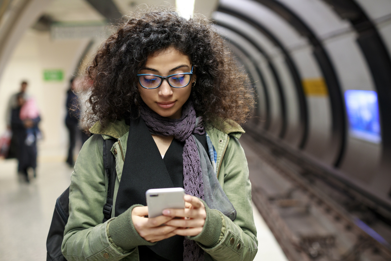 Giovane donna con cellulare in stazione della metropolitana
