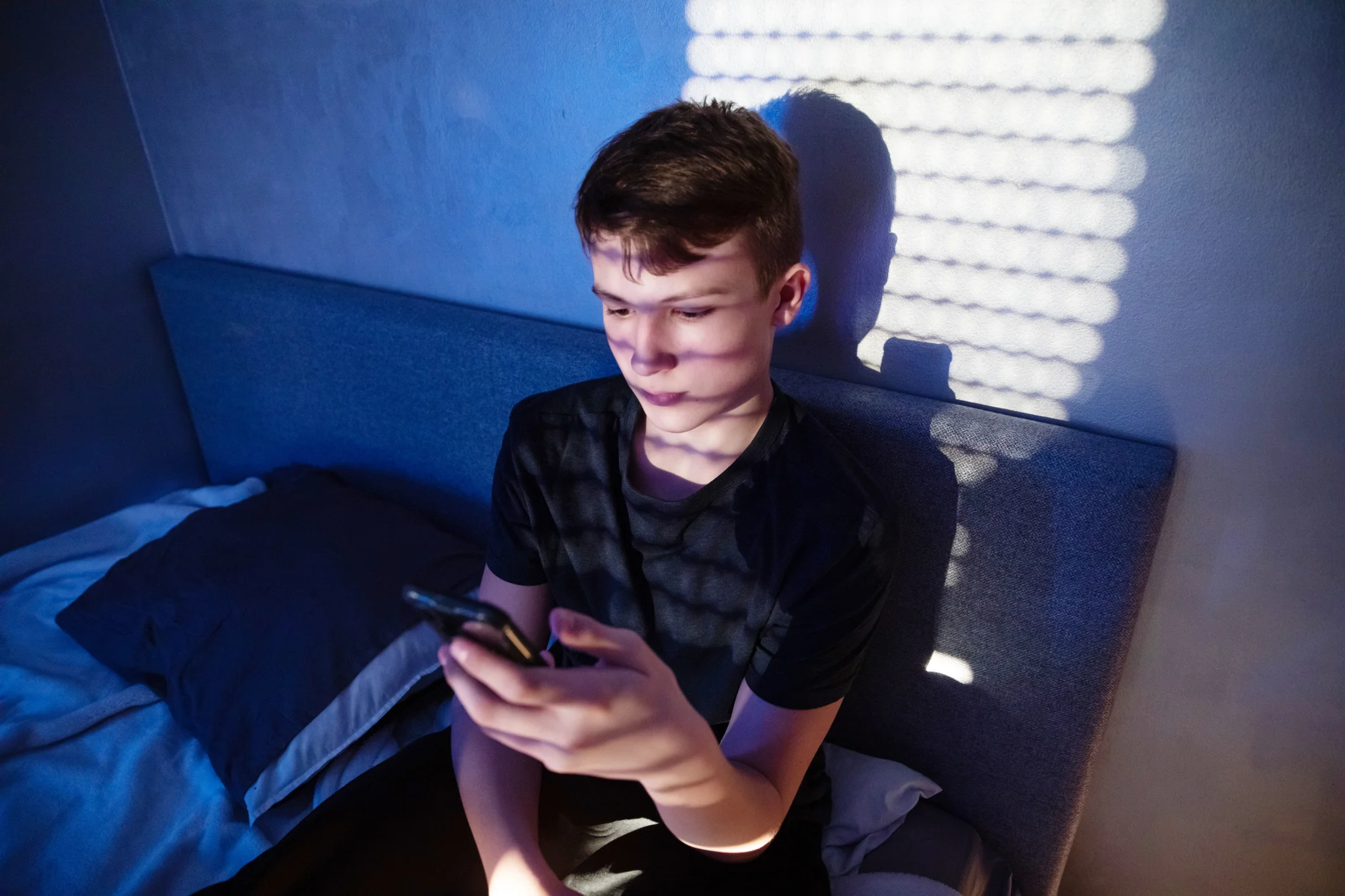 Un giovane uomo seduto sul letto guarda il cellulare