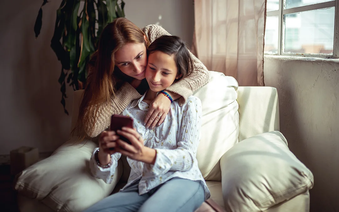 Mamma e figlia sedute sul divano guardano uno smartphone