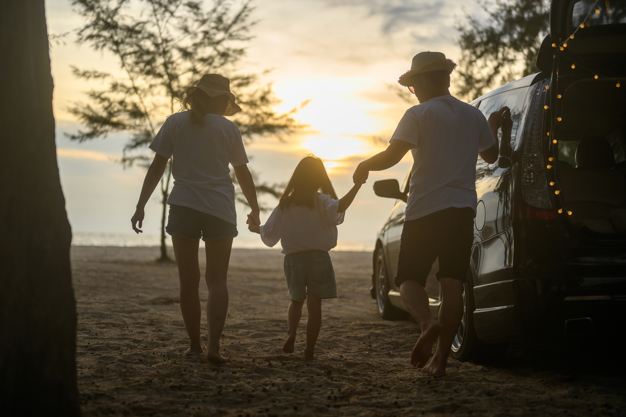 Un padre e una madre camminano verso il mare tenendo per mano la loro bambina