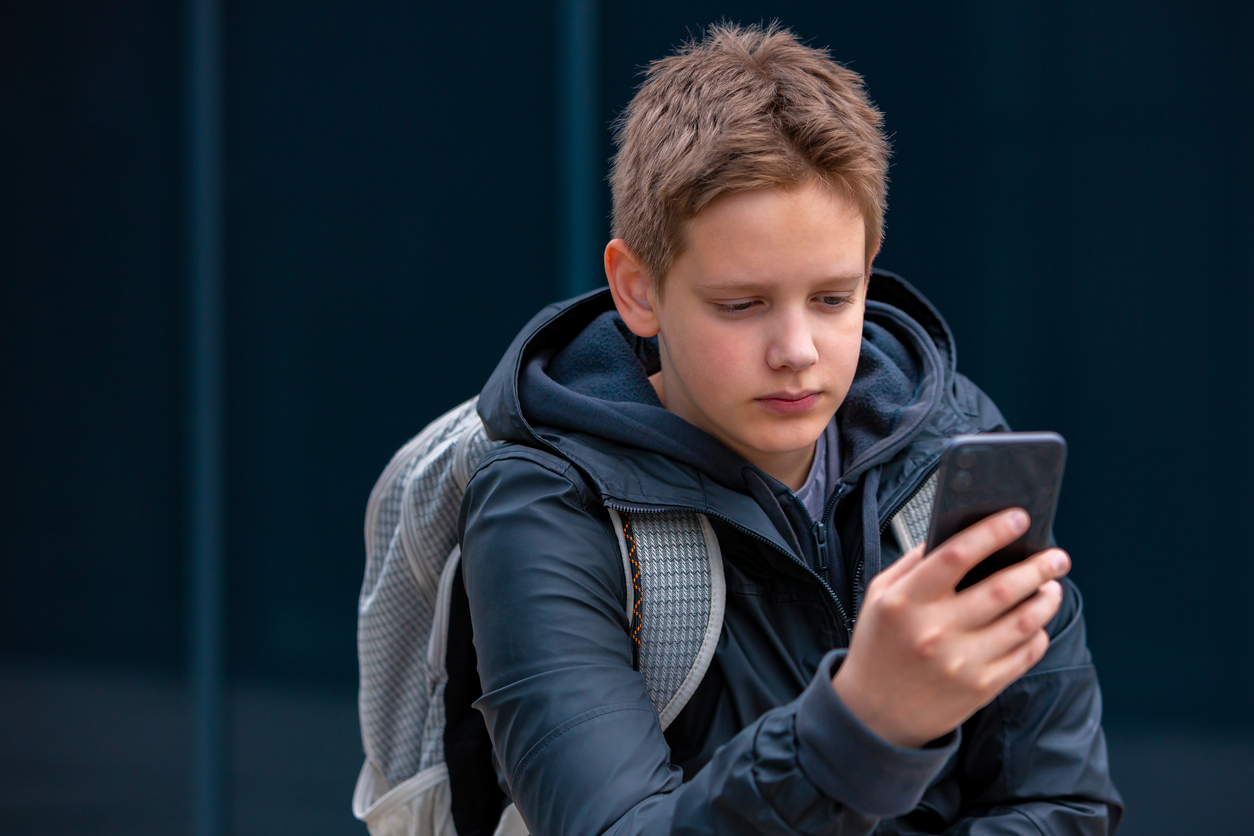 Un giovane studente adolescente in piedi all'aperto che guarda il telefono.
