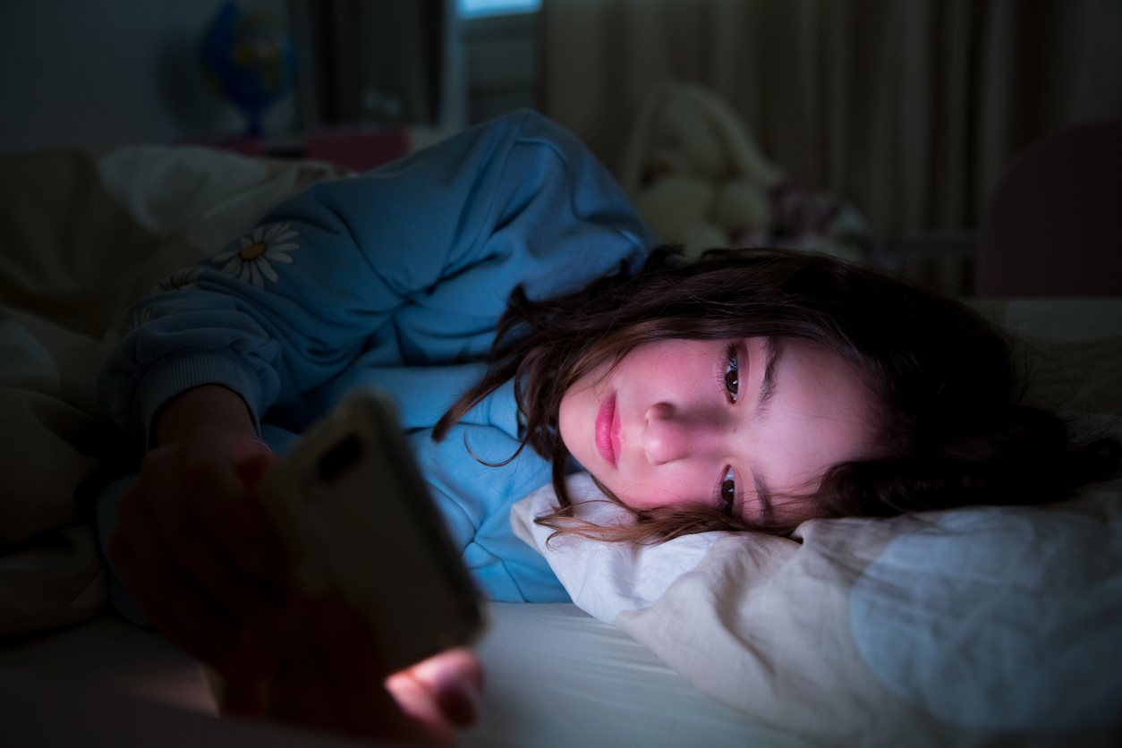 Preadolescente che usa lo smartphone sdraiata nel letto