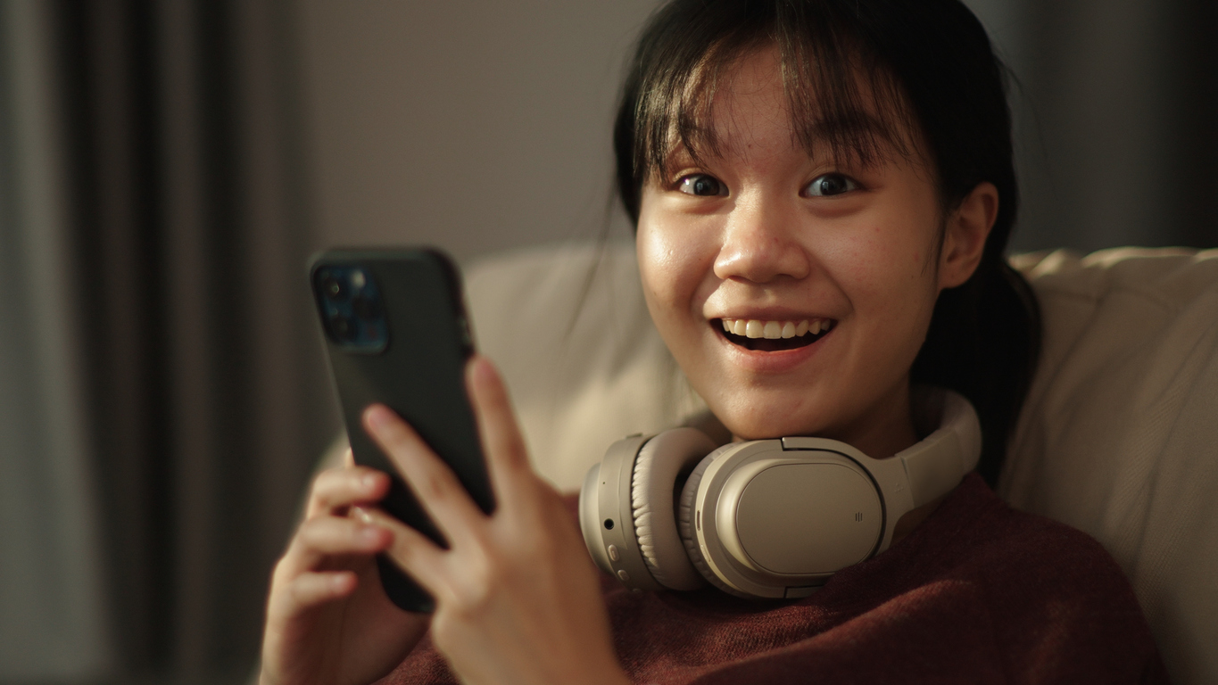 Ragazza asiatica guarda in camera felice con cellulare in mano