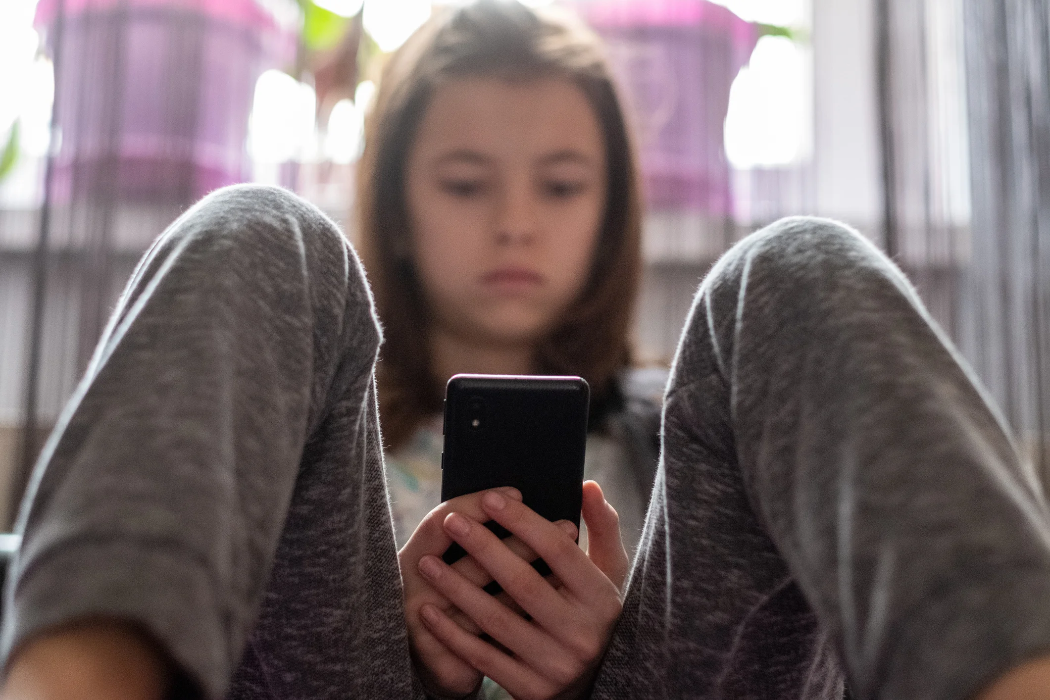 Una ragazzina seduta per terra guarda il suo smartphone