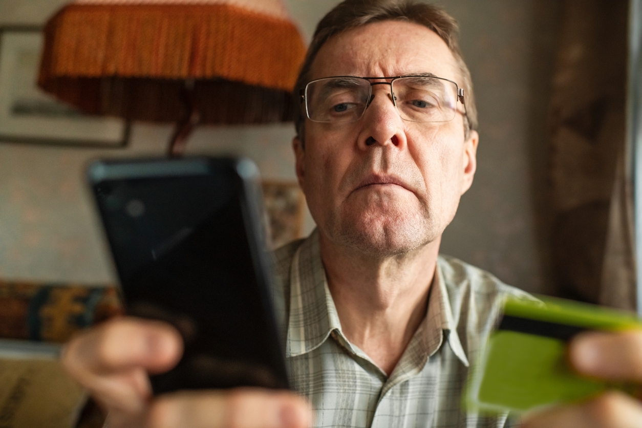 Uomo osserva schermo di un cellulare con carta di credito nell'altra mano