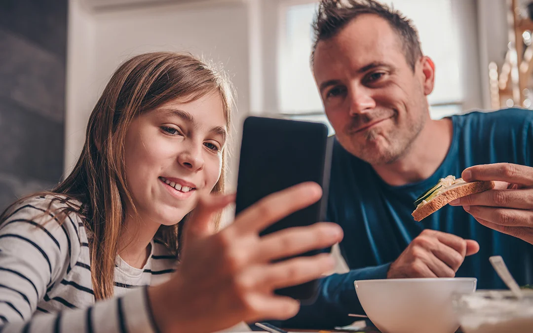 Un uomo e una ragazzina mangiano insieme con dispositivo digitale
