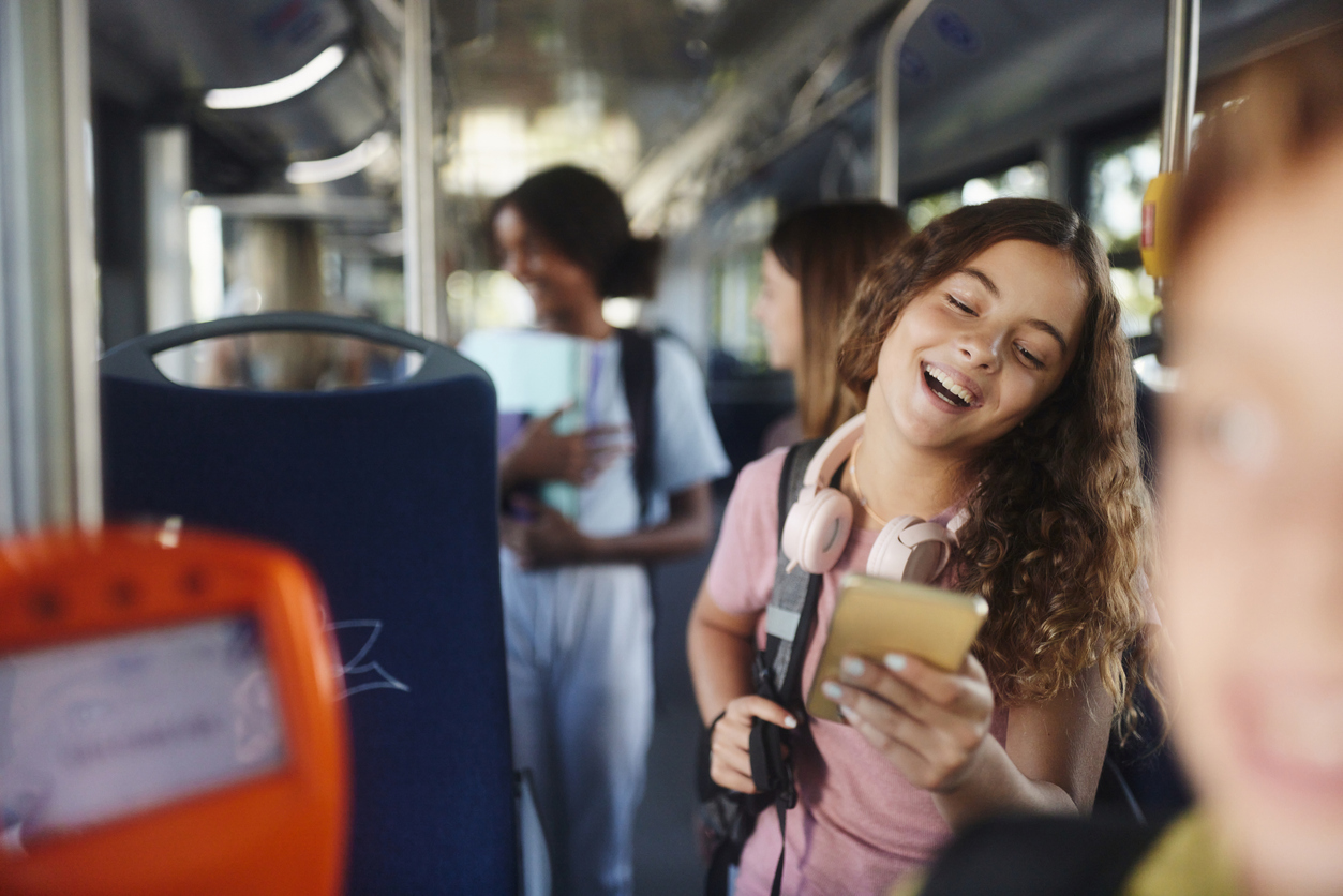 Studentessa felice che usa il cellulare mentre viaggia in autobus