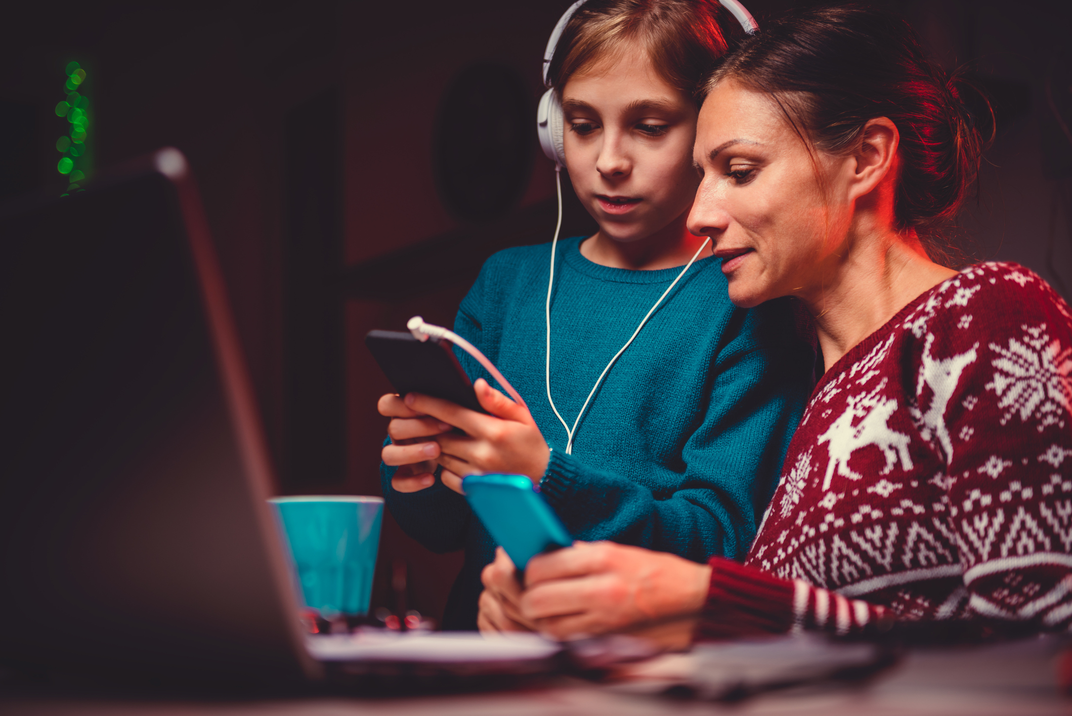 Una bambina con le cuffie e sua madre guardano un dispositivo digitale