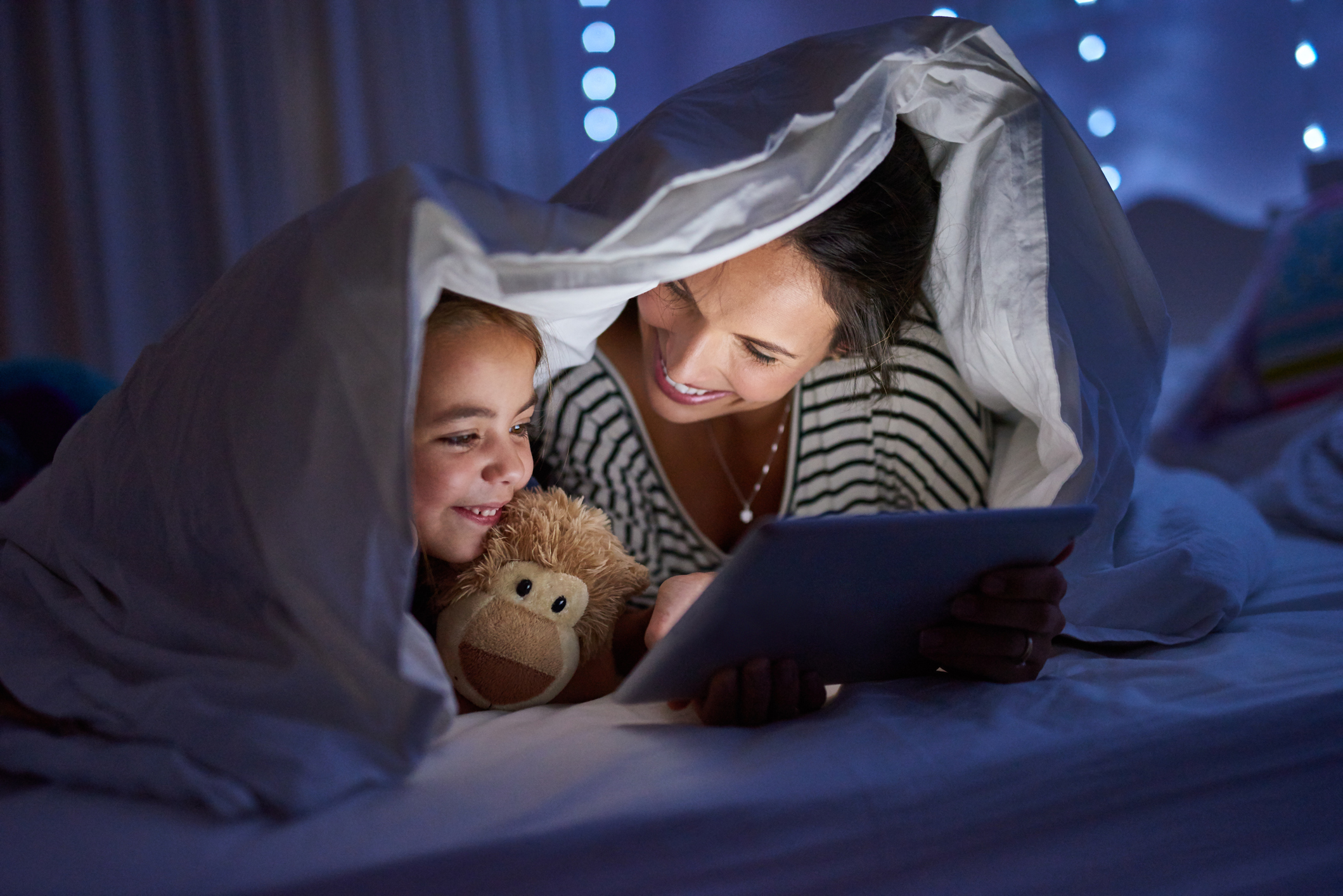 Una donna e una bambina sotto le coperte guardano un tablet
