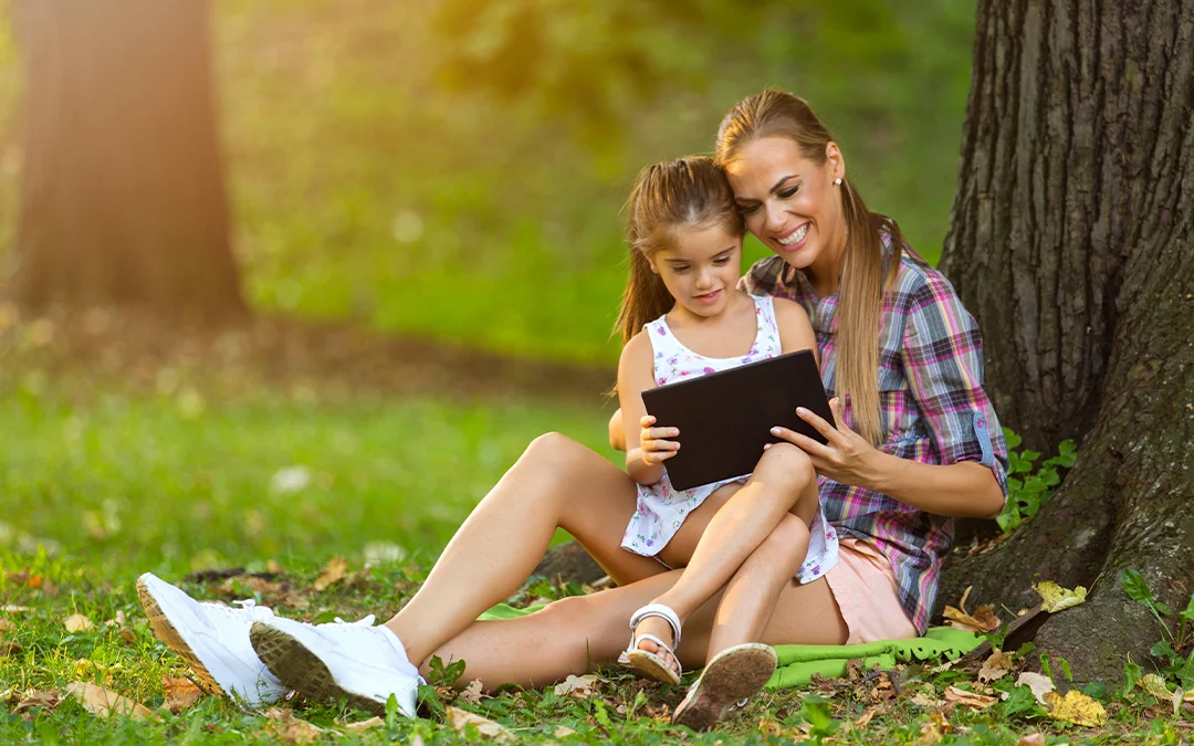 Una donna e una ragazzina sedute sotto un albero usano un tablet