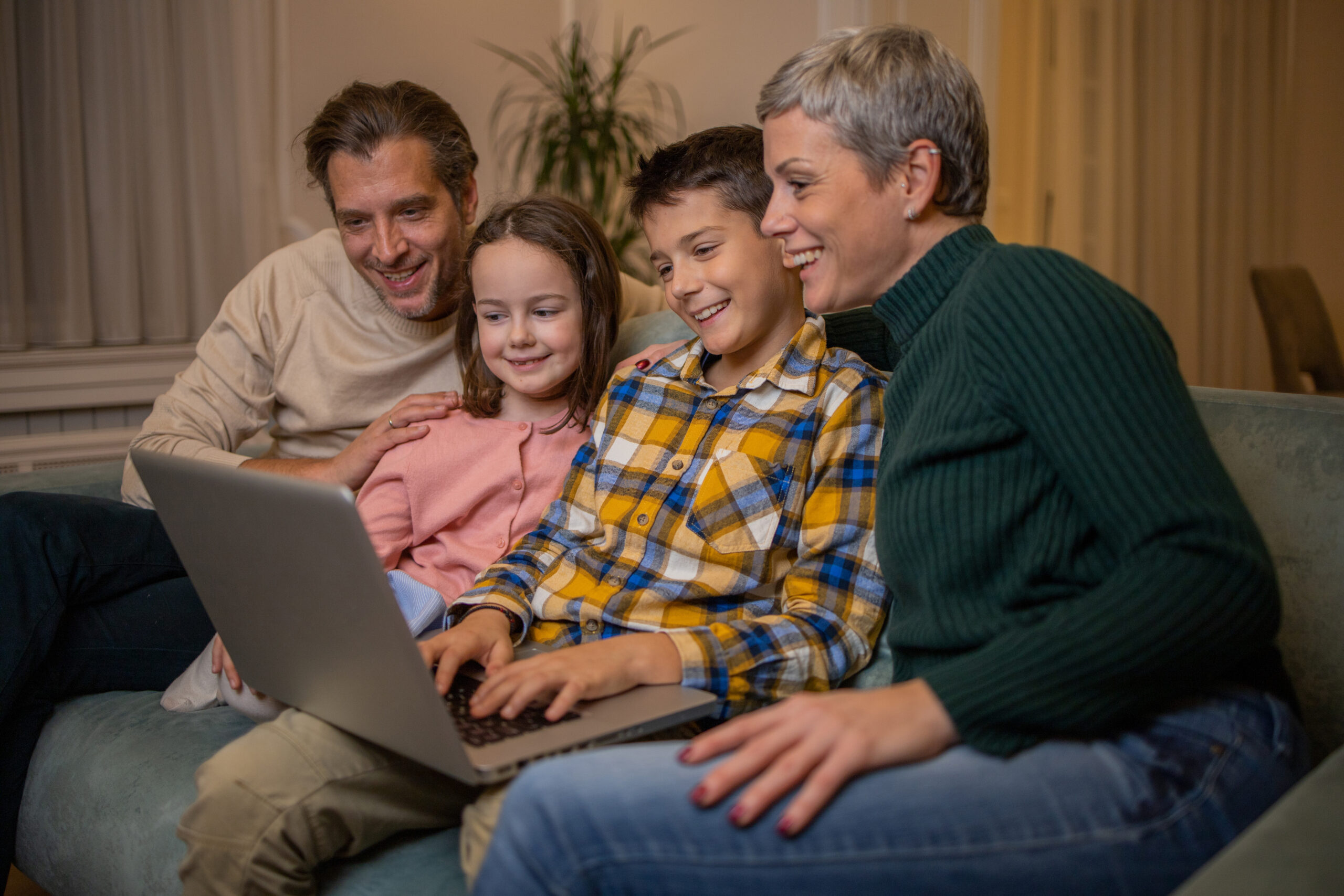 Famiglia con due bambini seduta sul divano a giocare al computer