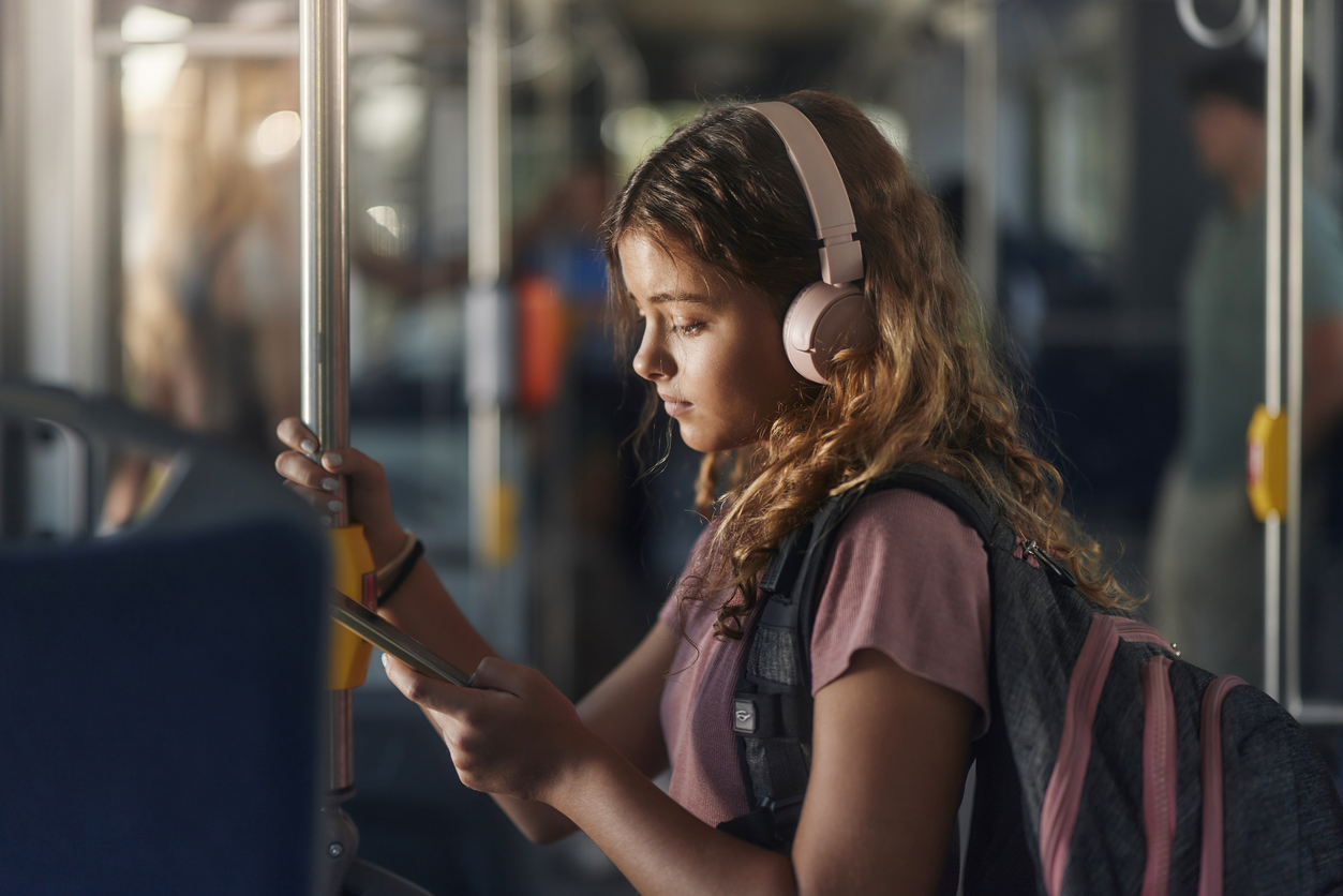 Studentessa sull'autobus ascolta musica con cuffie e smartphone