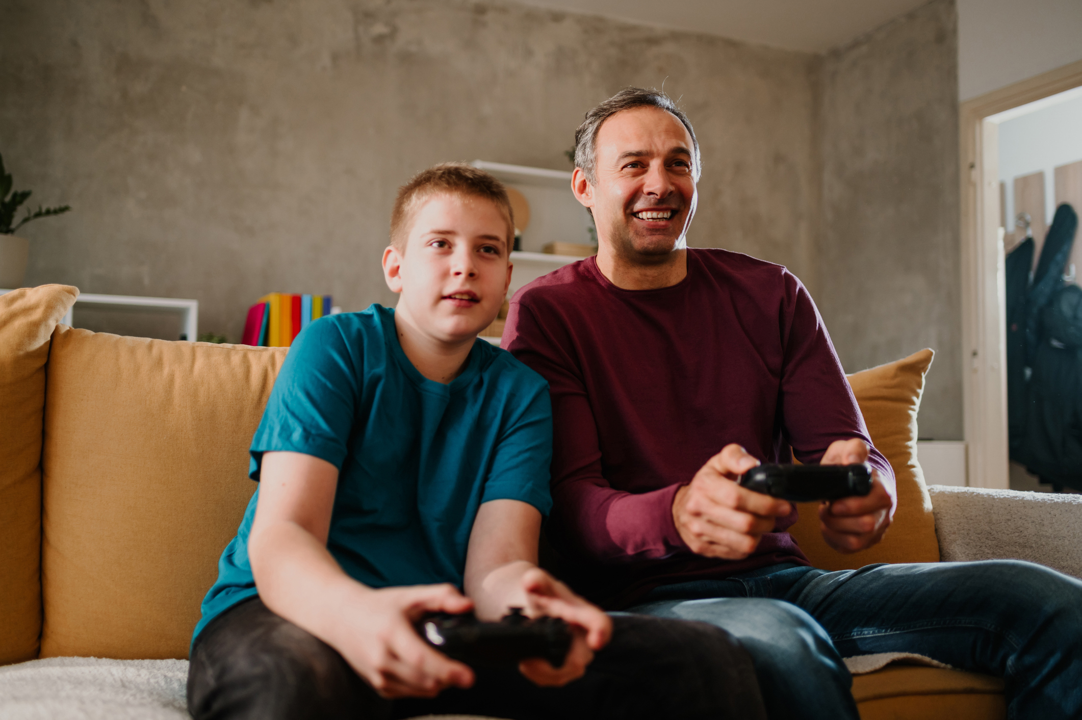 Un uomo e un ragazzino seduti sul divano giocano a un videogioco con dispositivo digitale